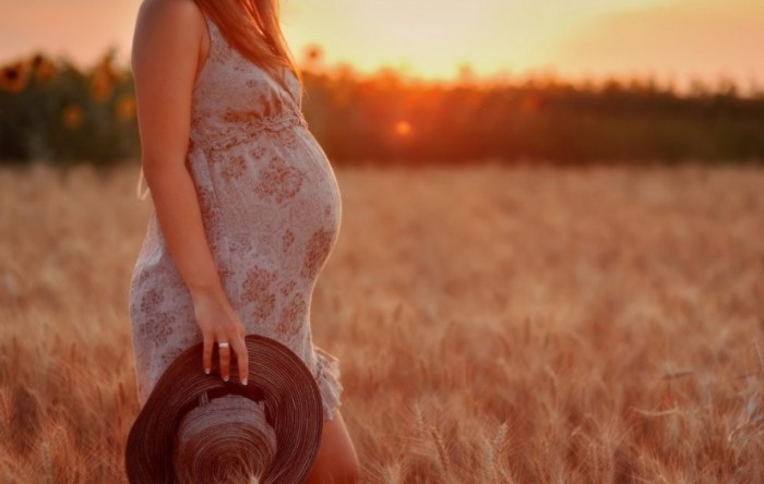 Беременная женщина гуляет в поле на закате солнца 